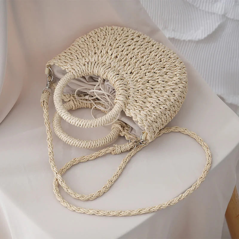 Bolso de paja tejida blanco roto con trenza larga sobre una superficie clara