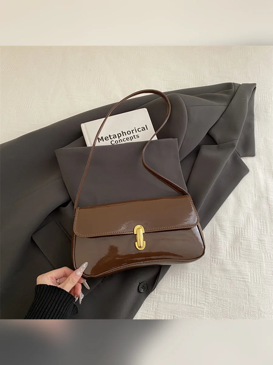 Bolso de hombro café brillante con cierre dorado sobre ropa gris