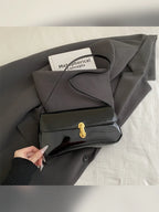 Bolso de hombro negro brillante con cierre dorado sobre ropa gris