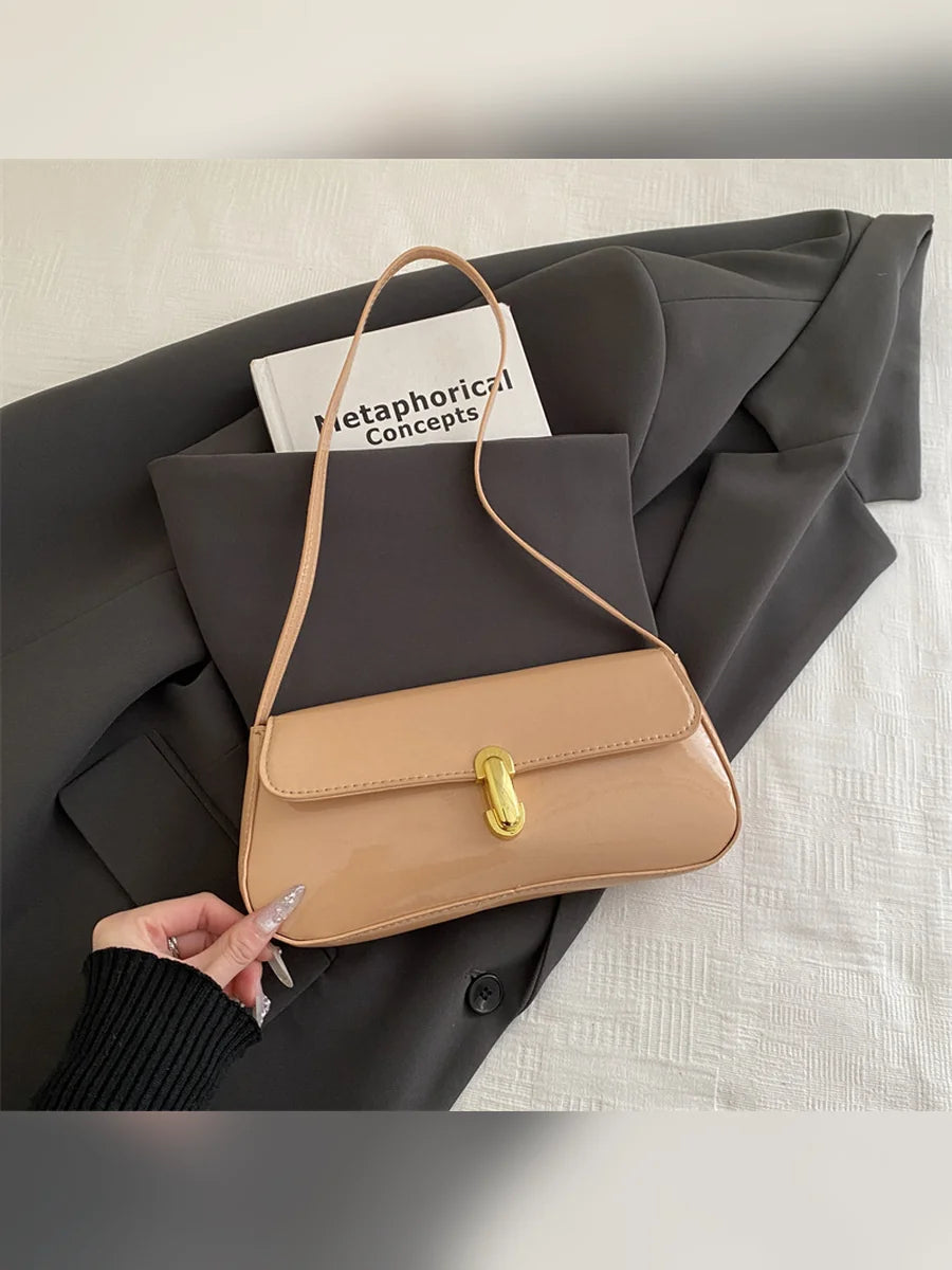 Bolso de hombro caqui brillante con cierre dorado sobre ropa gris