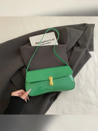 Bolso de hombro verde brillante con cierre dorado sobre ropa gris