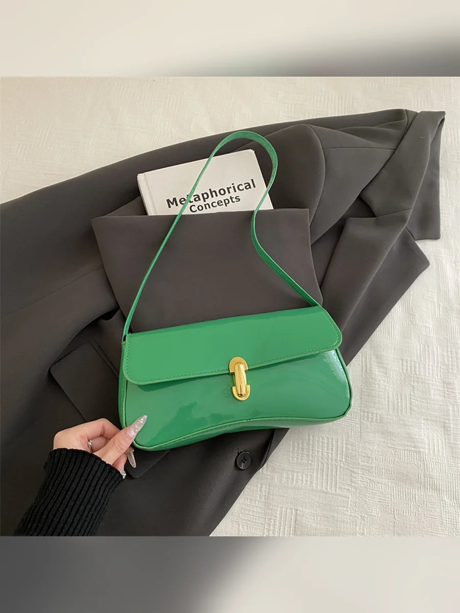 Bolso de hombro verde brillante con cierre dorado sobre ropa gris