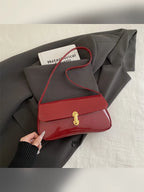 Bolso de hombro rojo brillante con cierre dorado sobre ropa gris