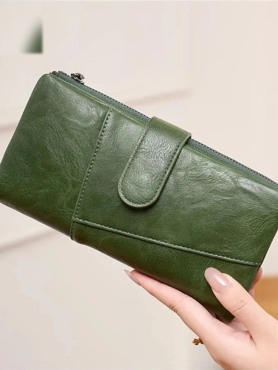 Cartera larga verde con hebilla y doble cremallera sostenida en la mano