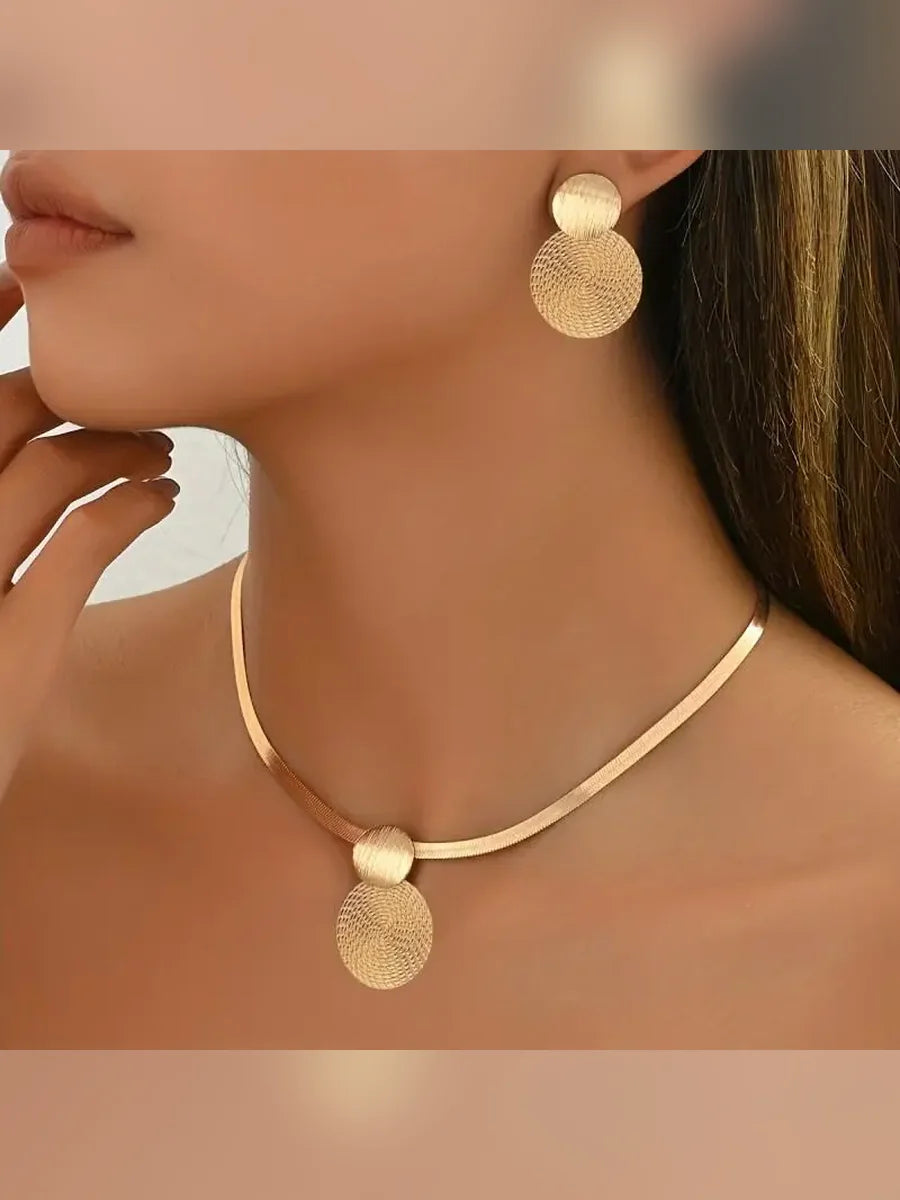 Mujer luciendo el collar de cadena plana dorada con colgante de disco y aretes a juego