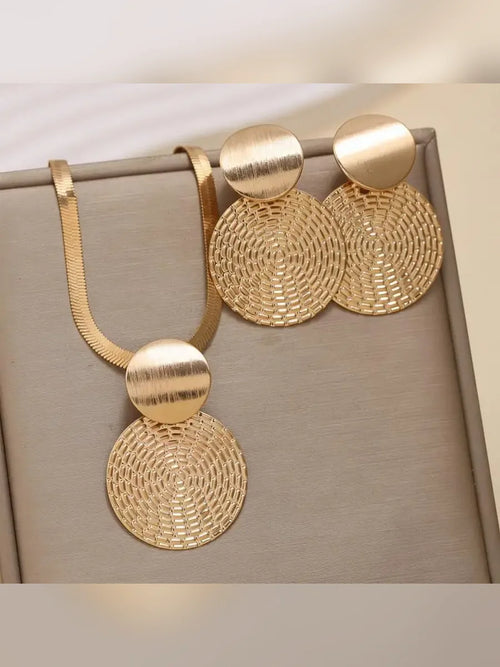 Set de collar y aretes de disco dorado con textura calada sobre fondo gris