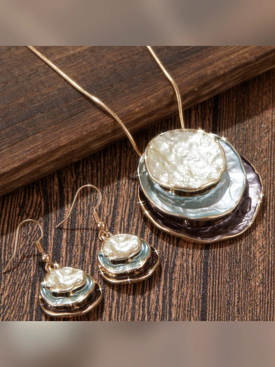 Dije circular esmaltado y aretes colgantes sobre madera oscura
