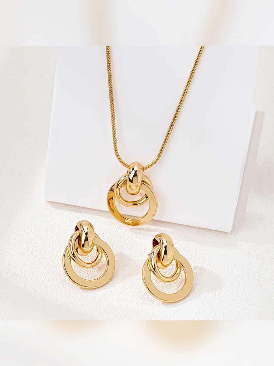Dije y aretes dorados de aros entrelazados sobre soporte blanco