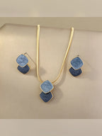 Set de collar y aretes con rombos esmaltados en azul sobre fondo beige