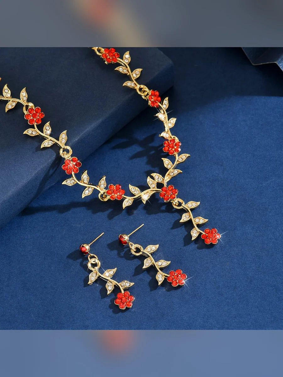 Detalle del collar dorado con flores rojas y aretes colgantes