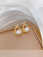 Aretes dorados de perla con cruz de cristales sobre fondo beige