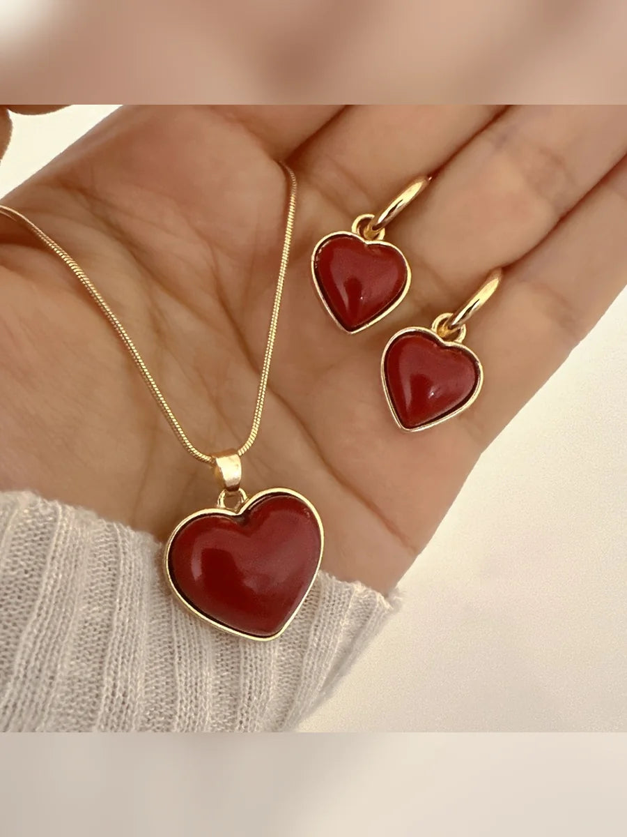 Mano mostrando el collar con corazón rojo y los aretes de aro a juego