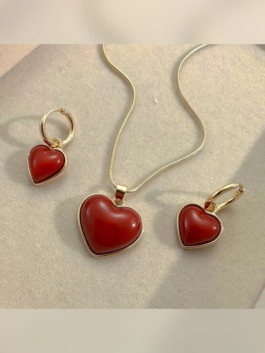 Collar y aretes con corazones rojos y borde dorado sobre fondo beige