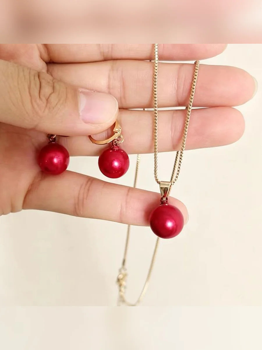Mano sosteniendo el set de collar y aretes con perlas rojas