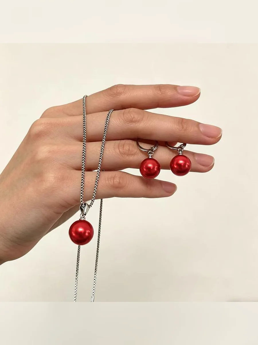 Mano sosteniendo el set plateado de collar y aretes con perlas rojas
