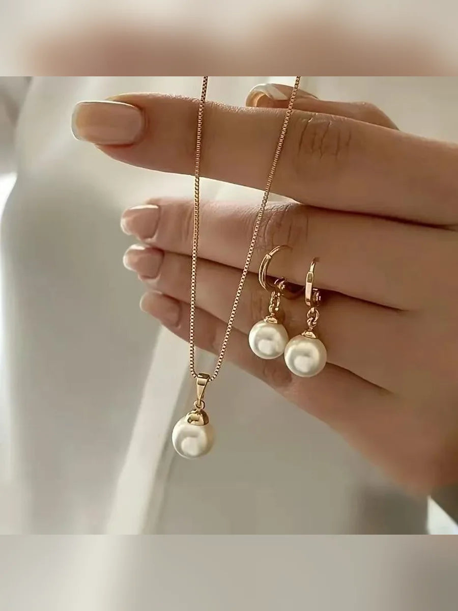 Mano mostrando el collar dorado con perla beige y aretes de aro a juego