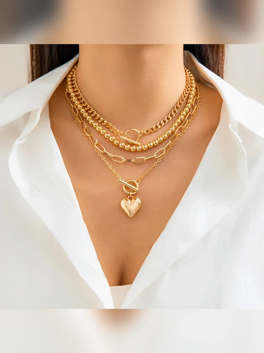 Collar multicapa dorado con dije de corazón sobre camisa blanca