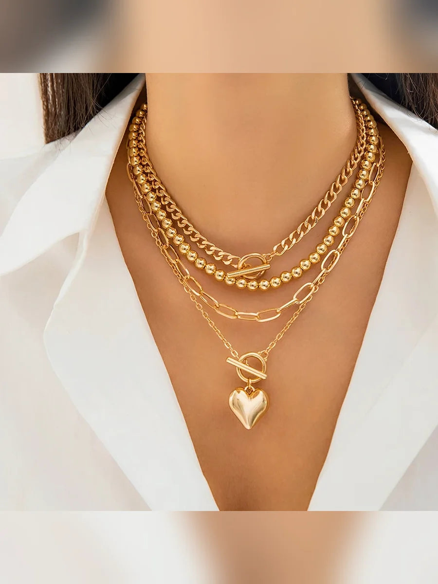 Mujer con collar multicapa dorado de cadenas y bolitas con dije de corazón