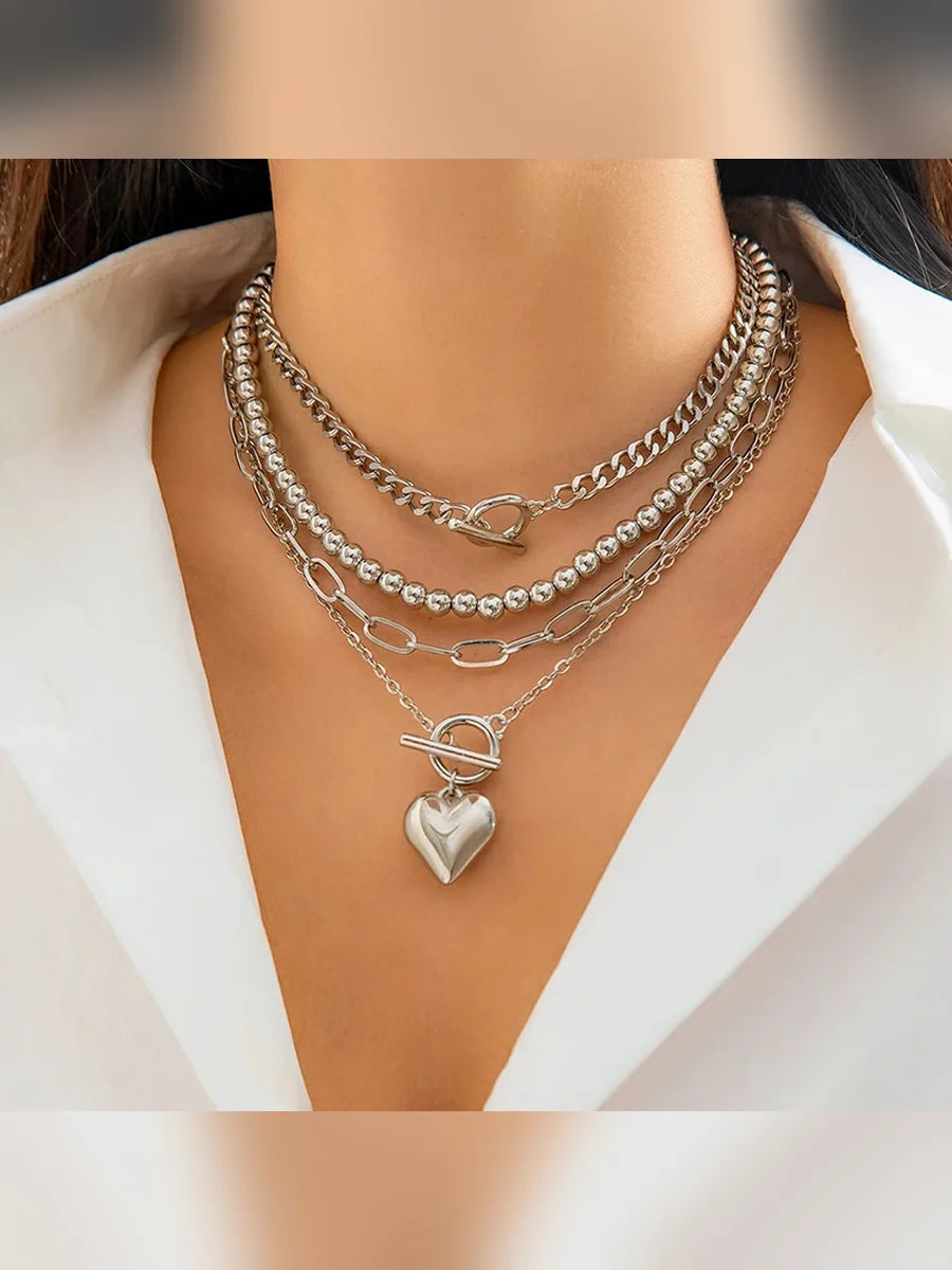 Collar multicapa plateado con dije de corazón sobre camisa blanca