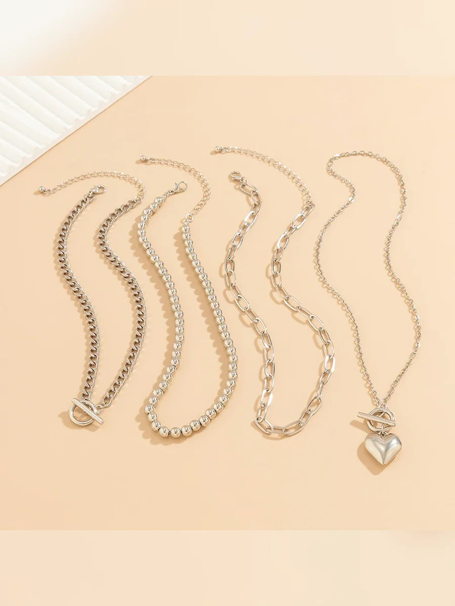 Cuatro cadenas plateadas del collar multicapa con dije de corazón sobre fondo beige