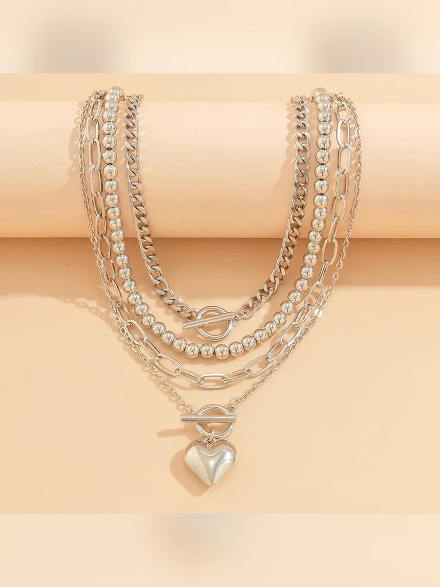 Collares plateados superpuestos con dije de corazón colgando sobre fondo rosado