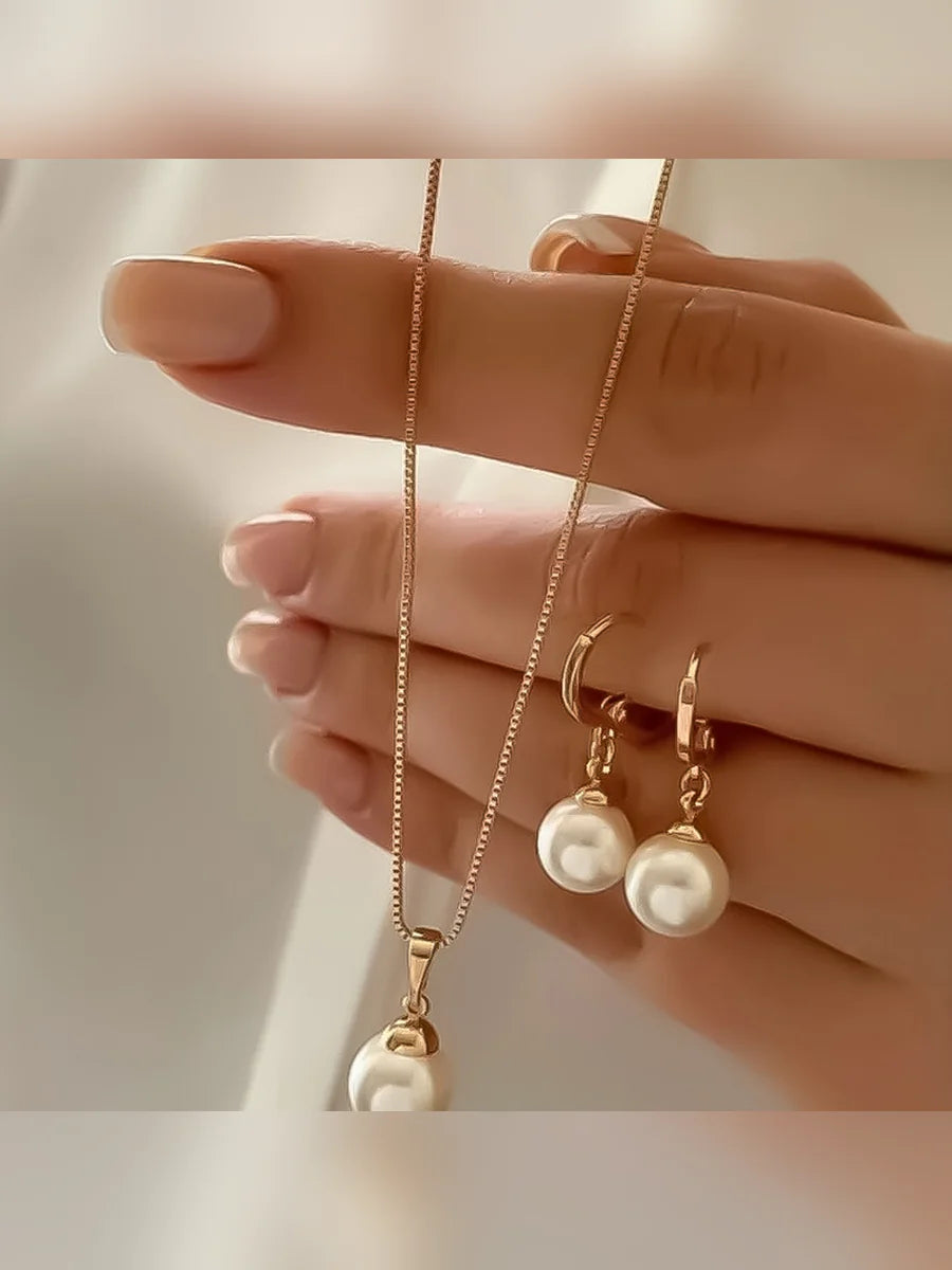 Mano mostrando el collar dorado con perla crema y los aretes de aro a juego