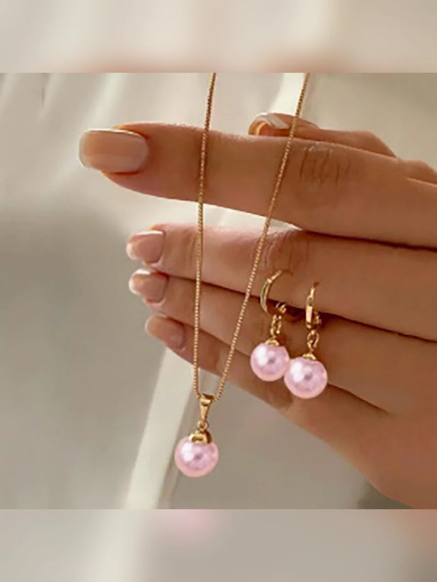 Mano mostrando el collar dorado con perla rosa y los aretes de aro a juego