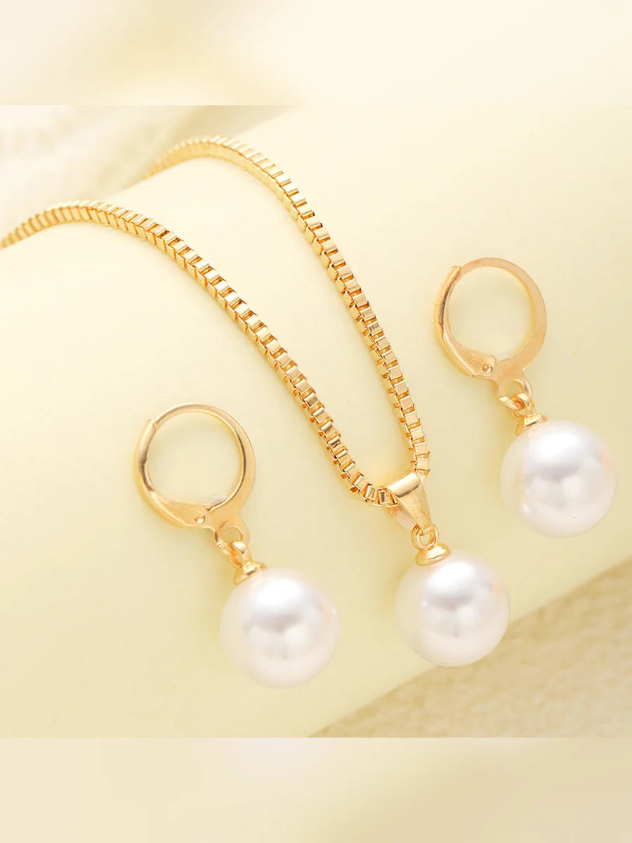 Collar dorado con dije de perla y aretes de aro sobre tela clara