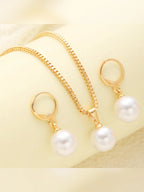 Collar dorado con dije de perla y aretes de aro sobre tela clara