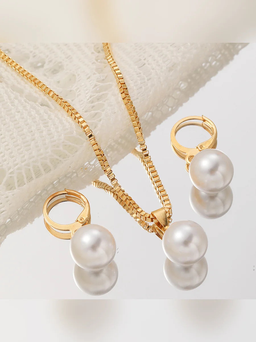 Aretes de aro con perla y collar de cadena dorada sobre tejido blanco