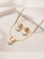 Dije de disco dorado con corazón nacarado y aretes sobre superficie blanca