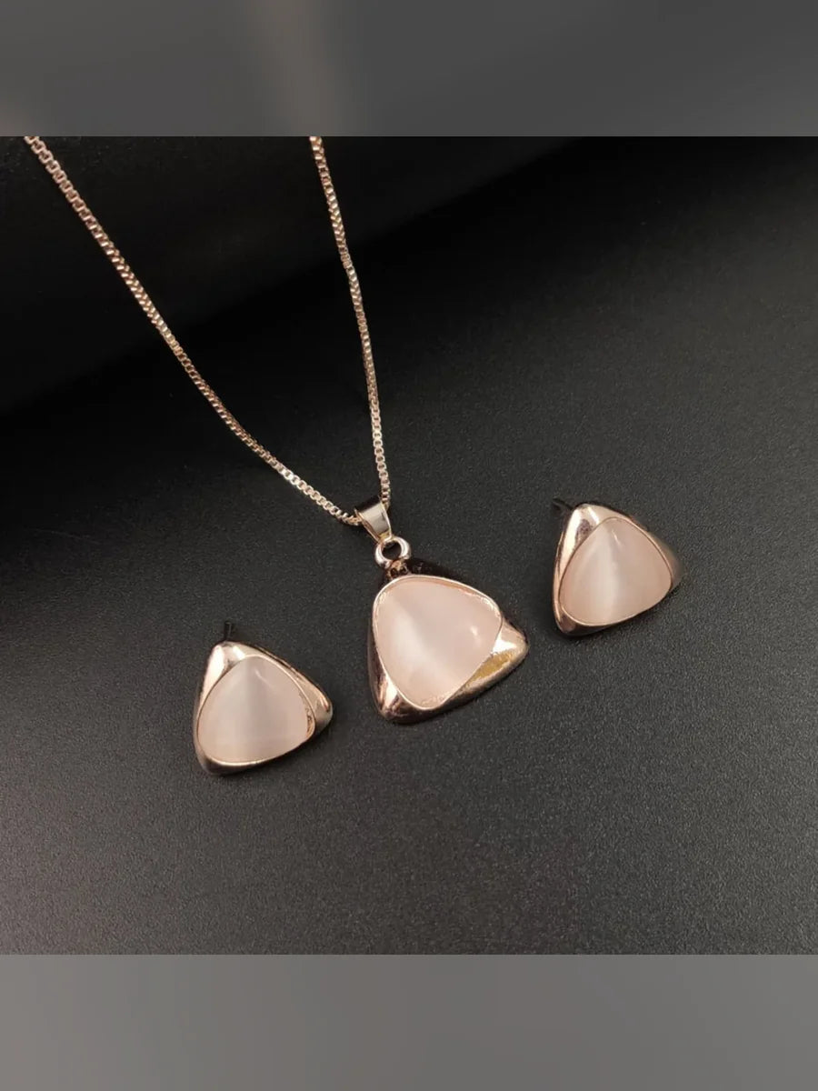 Dije y aretes triangulares de ojo de gato rosa sobre fondo oscuro